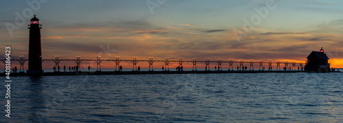 Grand Haven Lighthouse Michigan on Lake Michigan at sunset during the winter with beautiful colors and the structures and people silhouetted.  Hot from North Pier.
