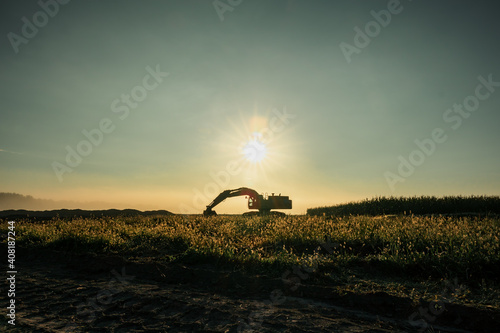 An excavator sits under the rising sun as the fog gently lifts from the ground.