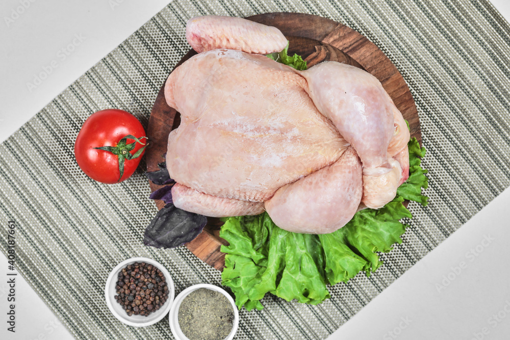 Raw whole chicken on wooden plate with lettuce, tomato and spices Raw whole chicken on wooden plate with lettuce, tomato and spices