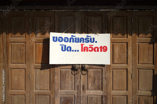shop or store sign with wording in Thai language meaning " sorry. closed...covid 19 " hanging on the door 