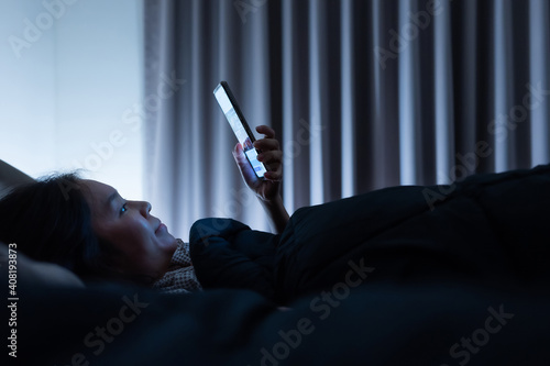 Asian woman on bed late at night and using mobile smartphone before sleep in dark bedroom photo