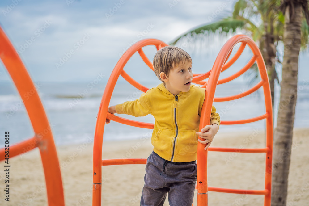 The boy climbs on the playground against the background of palm trees The boy climbs on the playground against the background of palm trees