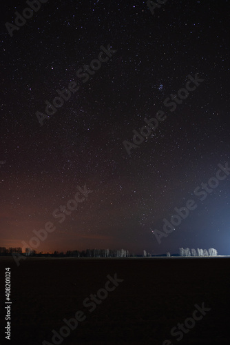 Starry sky over the forest near the field in the distance