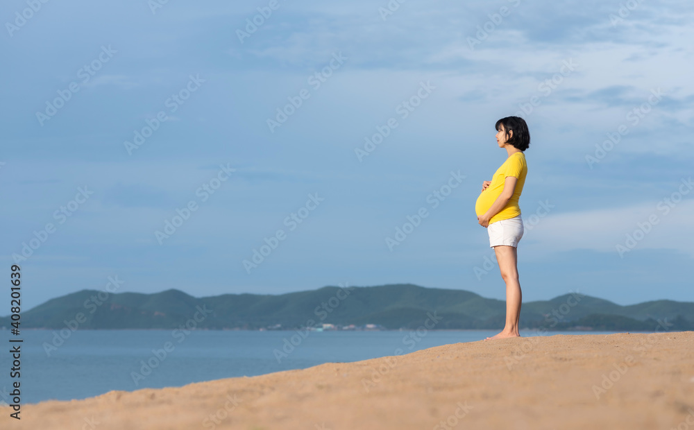 Asian Pregnant woman standing breathing fresh air and holding touching her belly on the beach outdoor. Asian Pregnant woman standing breathing fresh air and holding touching her belly on the beach outdoor.