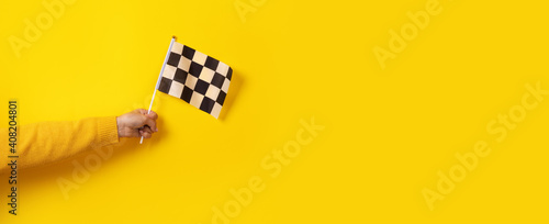 checkered flag in hand over yellow background, panoramic image photo