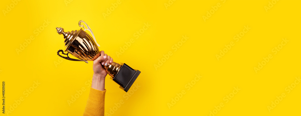 woman holding up a gold trophy cup as a winner in a competition, panoramic image - obrazy, fototapety, plakaty 