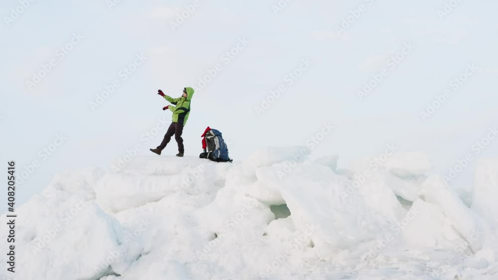 Panoramic view from below of a happy woman in green jacket dancing on big icy blocks against the blue sky. Winter Panoramic view from below of a happy woman in green jacket dancing on big icy blocks against the blue sky. Winter