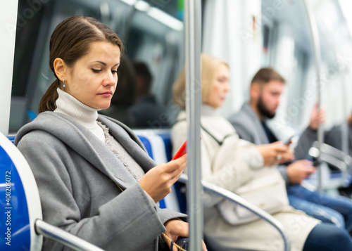 Young focused woman browsing and typing messages on phone on way to work in modern metro car