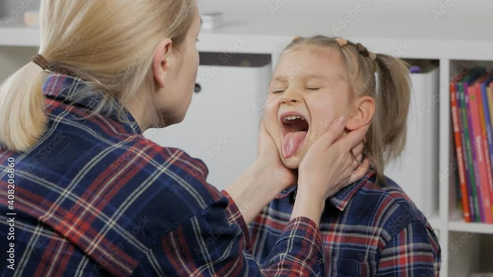 A mother examines her little daughter's throat while sitting at home in the nursery A mother examines her little daughter's throat while sitting at home in the nursery