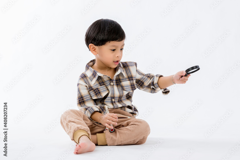 Child holding magnifying glass on white background. Boy with a magnifying glass in studio. Positive curious boy in casual wear looking at through magnifier Child holding magnifying glass on white background. Boy with a magnifying glass in studio. Positive curious boy in casual wear looking at through magnifier