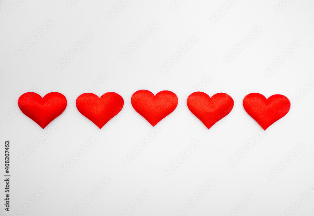 Five textured red hearts line up one after the other on a white or gray background: St. Valentine's Day background with place for text, minimalism 
