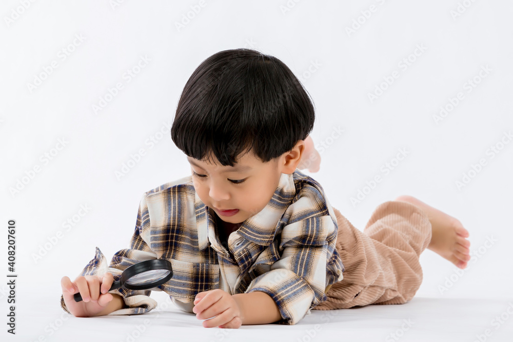 Child holding magnifying glass on white background. Boy with a magnifying glass in studio. Positive curious boy in casual wear looking at through magnifier Child holding magnifying glass on white background. Boy with a magnifying glass in studio. Positive curious boy in casual wear looking at through magnifier