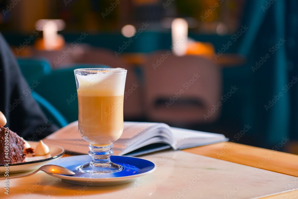 A cup of freshly brewed coffee latte on a table with a book and a piece of chocolate cake. Still life. Copy space banner