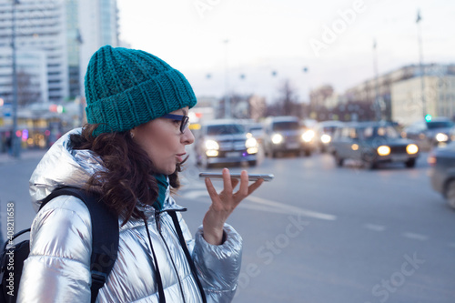 Send a voice message in messenger. A young woman in a down jacket and hat speaks on the phone, communication on the Internet