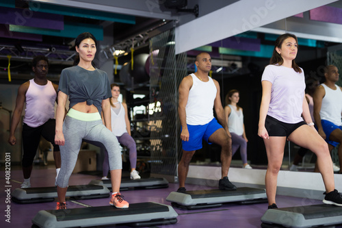 Multiethnic group of young adults training on step platforms in gym