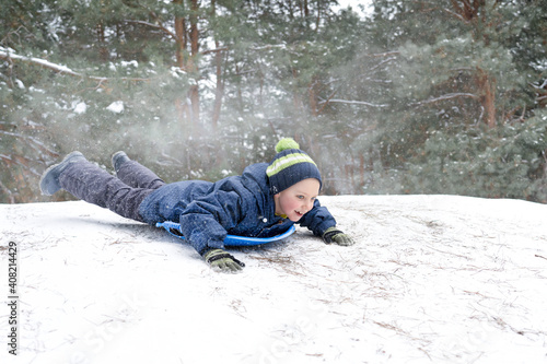 Boy sledding in a snowy forest. Outdoor winter fun for Christmas vacation.