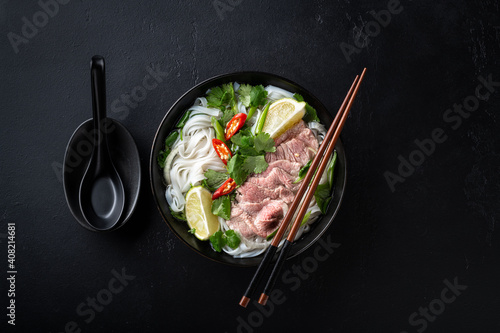 Pho Bo vietnamese soup with beef and rice noodles on a black background, top view
