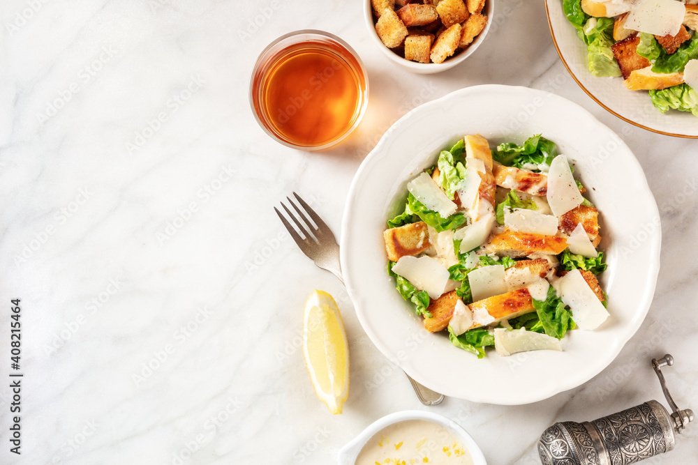 Caesar salad with the classic sauce and wine, overhead flat lay shot on a white marble background with copy space