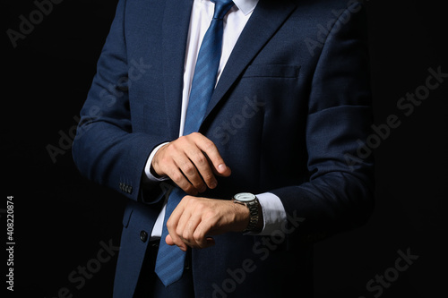 Young businessman with stylish wristwatch on dark background