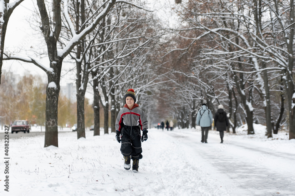 Child walks in winter snow-covered park. Little boy on a walk