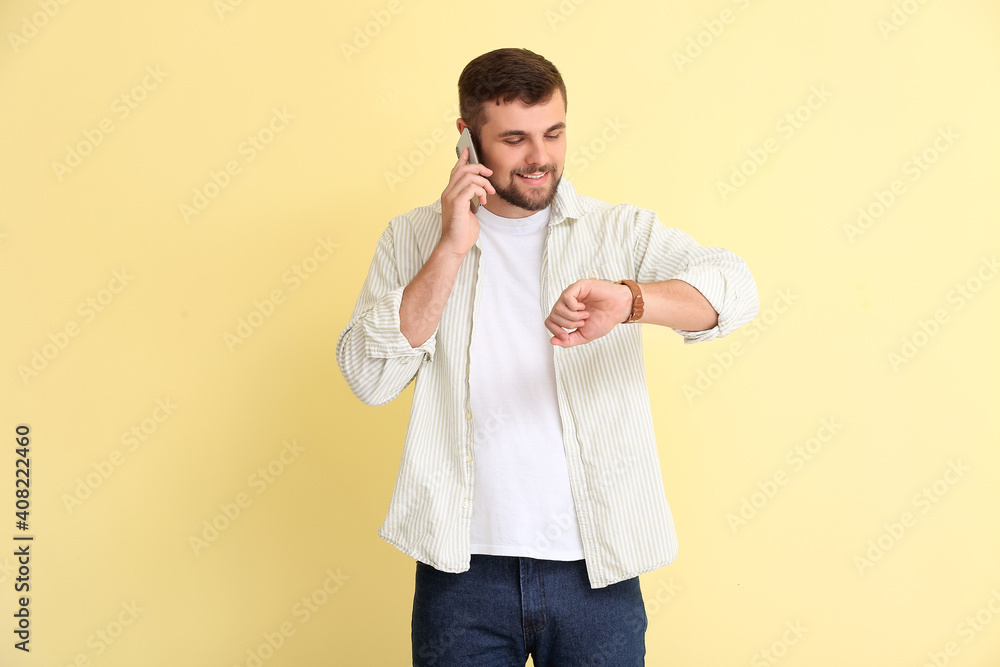 Handsome man looking at wristwatch and talking by mobile phone on color background Handsome man looking at wristwatch and talking by mobile phone on color background