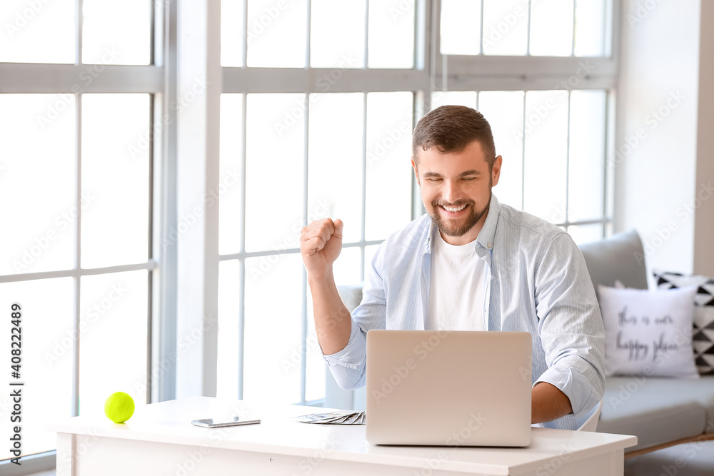 Happy man with laptop after winning his sports bet at home Happy man with laptop after winning his sports bet at home