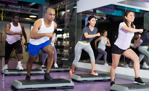 Group of sporty people working out with steppers in fitness center