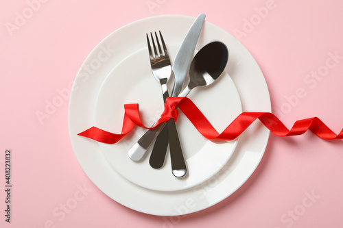 Plates with cutlery and red bow on pink background