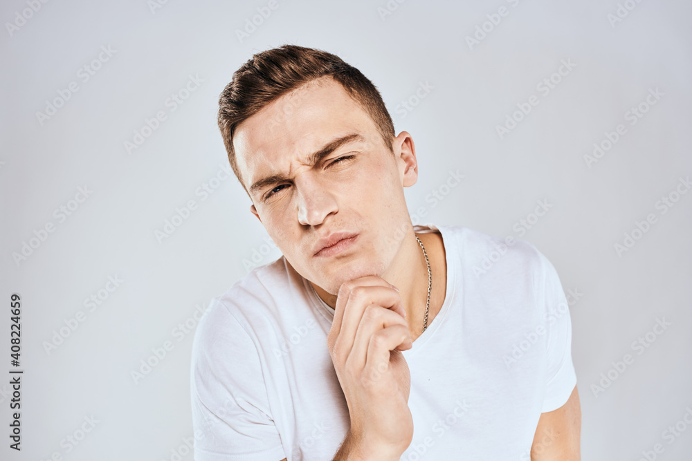 Emotional man in a white t-shirt holds his hand on his face light background Emotional man in a white t-shirt holds his hand on his face light background