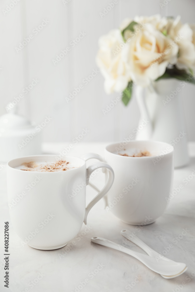 Two white porcelain cups of coffee. Bouquet of delicate cream flowers in the background. Romantic morning for two. Two white porcelain cups of coffee. Bouquet of delicate cream flowers in the background. Romantic morning for two.