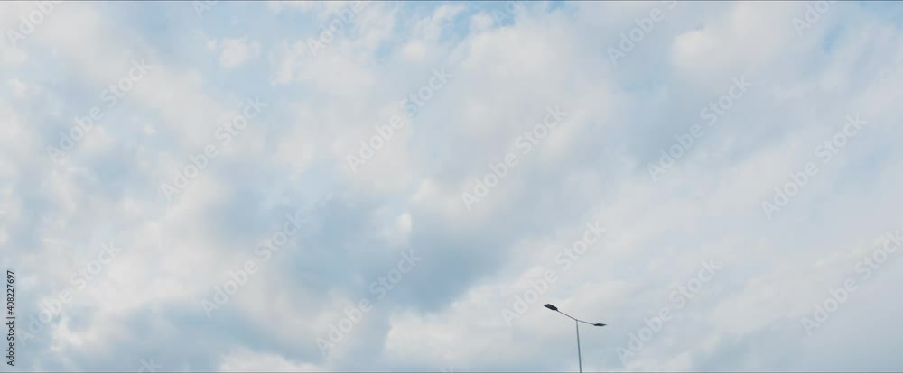 Camera tilted up to overcast sky while driving in town. Moving street light lamps against clouds. Car driver's point of view. Camera tilted up to overcast sky while driving in town. Moving street light lamps against clouds. Car driver's point of view.