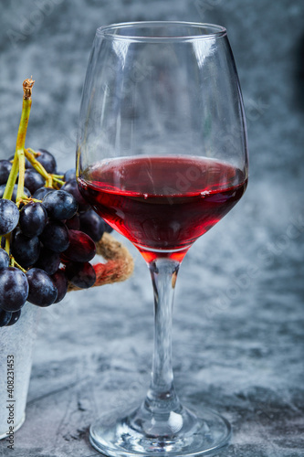A glass of red wine on a marble background with grapes