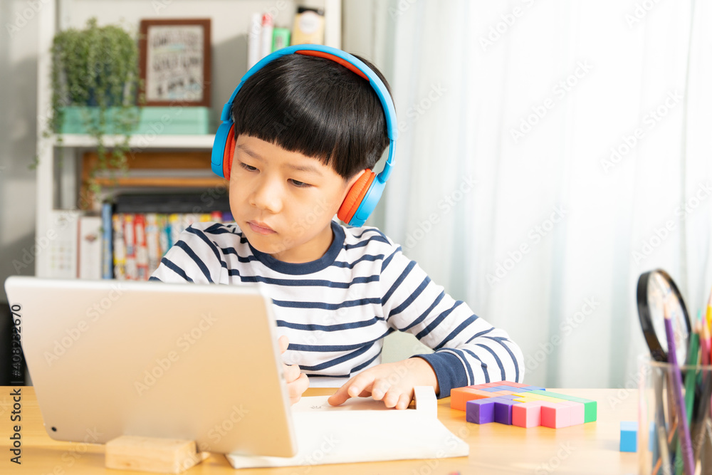 Portrait of smart Asian student boy with headphone, take note, study at home with tablet computer in online classroom during Covid-19 pandemic lockdown. New normal in technology, education, homeschool Portrait of smart Asian student boy with headphone, take note, study at home with tablet computer in online classroom during Covid-19 pandemic lockdown. New normal in technology, education, homeschool