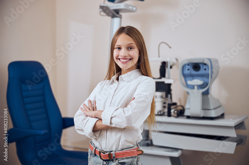 Happy cheerful female child standing in front of the modern machine for checking eyesight