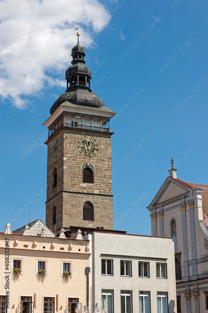 traditional European buildings and a tower with a copper dome and a clock on a sunny day in Jicin, Czech Republic.