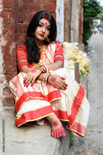 Portrait of beautiful Indian woman wearing traditional Indian saree, gold jewellery and bangles sitting in front of vintage window beside a colony road in Calcutta. Lifestyle Expression and Fashion.