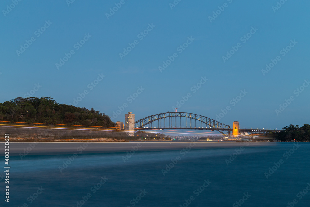 Obraz premium Boat travelling in front of Sydney Harbour Bridge at dusk.