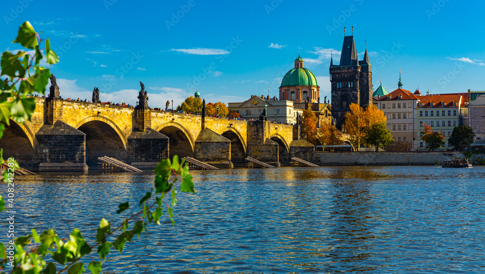 Obraz premium Scenic view of autumn Prague cityscape and ancient stone Charles Bridge across Vltava River on sunny day, Czech Republic