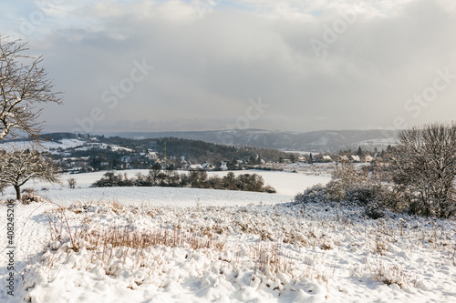 Beautiful winter sunny landscape with snowy hills, winter nature in the village, field and trees in the snow