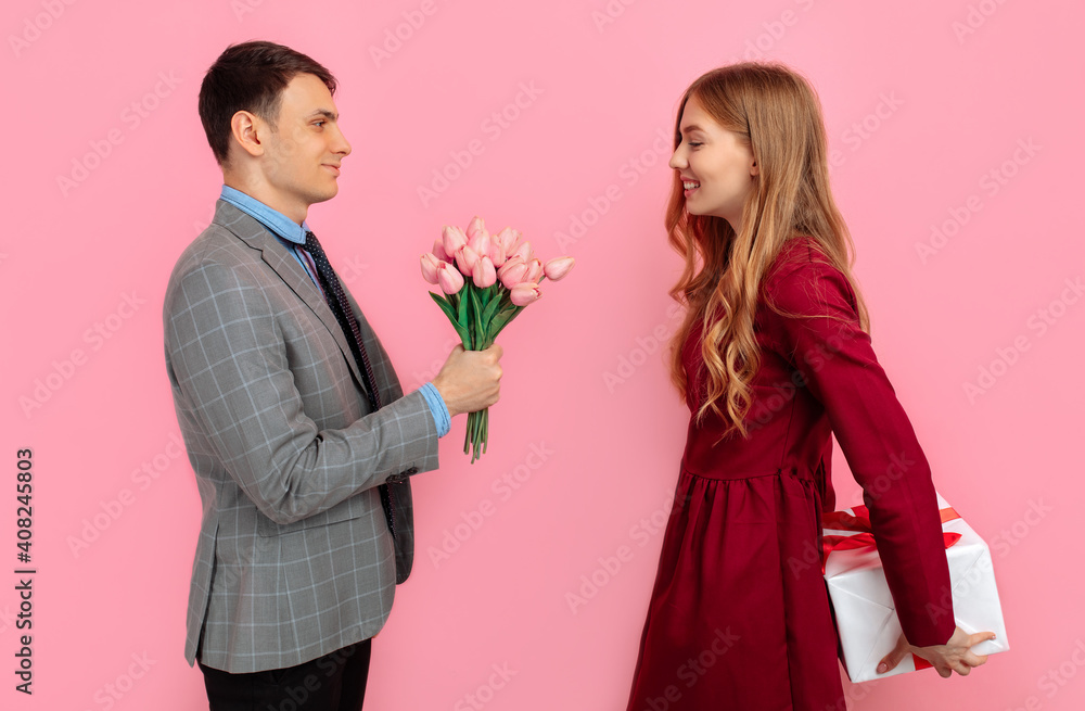 romantic couple, attractive young woman in a red dress makes a gift for her man in a suit, on a pink background, Happy Valentine's Day romantic couple, attractive young woman in a red dress makes a gift for her man in a suit, on a pink background, Happy Valentine's Day