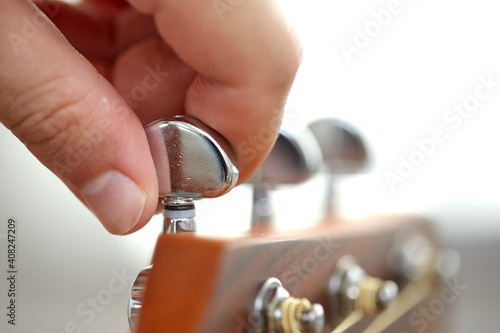 music and musical instruments concept - close up of hand tuning guitar strings with pegs