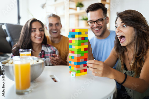Group of young happy friends having fun playing wood board game