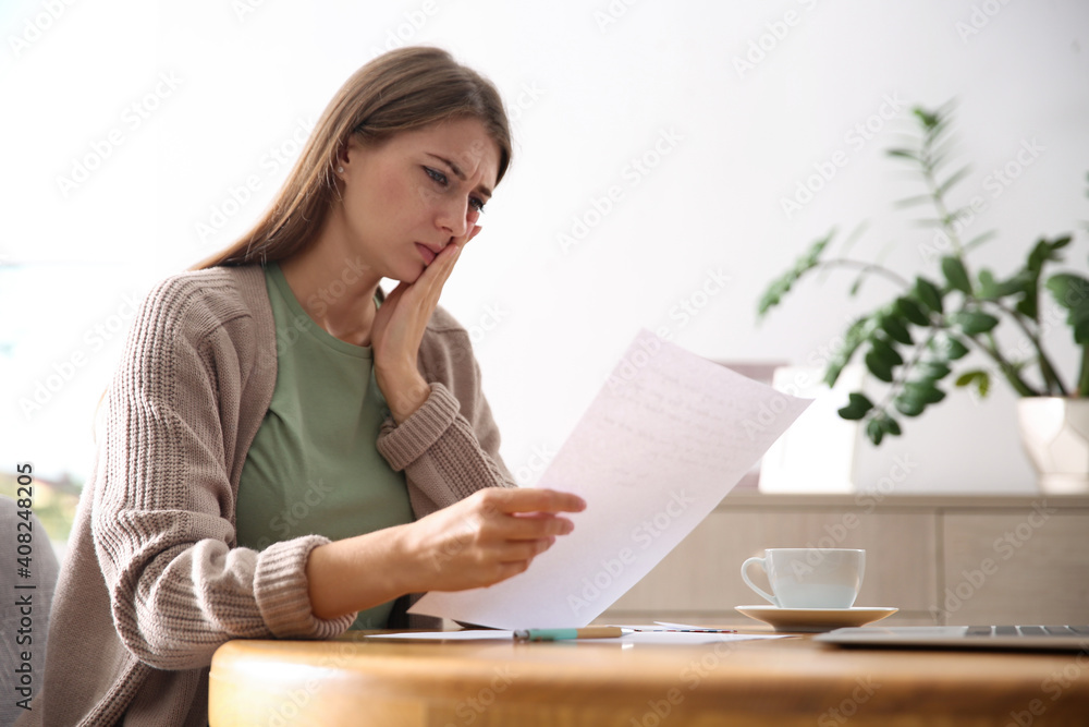 Worried woman reading letter at wooden table in room Worried woman reading letter at wooden table in room