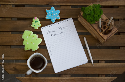 A notebook with plans for the new year, around the notebook are cookies in the form of Christmas trees and a cup of coffee