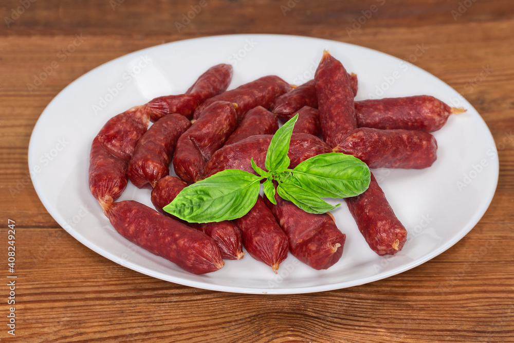 Small thin dry cured sausages with basil on a dish Small thin dry cured sausages with basil on a dish