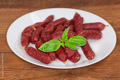 Small thin dry cured sausages with basil on a dish