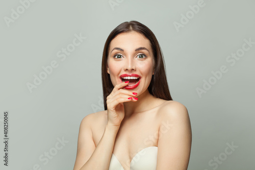 Portrait of cute surprised woman with healthy skin and red manicure on white background