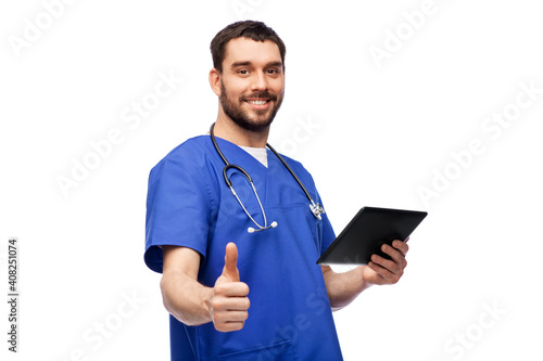 medicine, healthcare and technology concept - happy smiling doctor or male nurse in blue uniform with stethoscope using tablet pc computer and showing thumbs up over white background