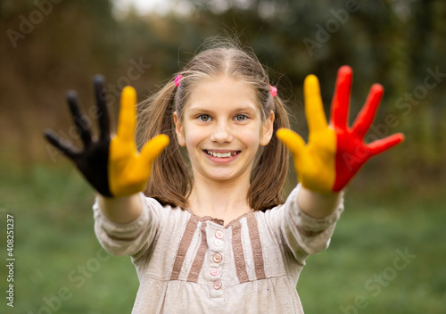 Happy outdoor portrait of child girl with hands painted in Belgium flag colors. Creative