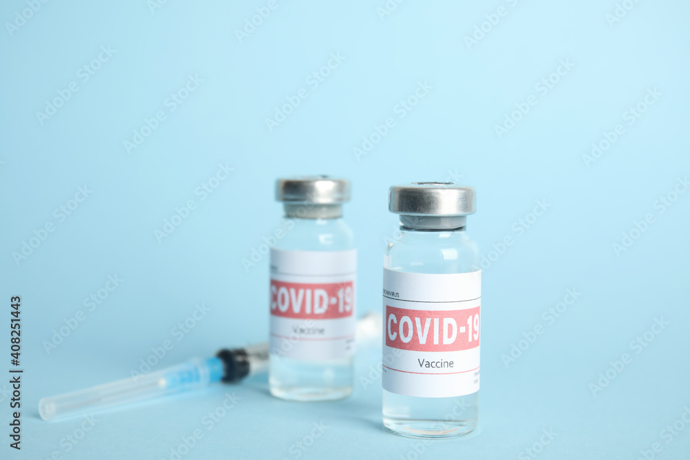 Vials with coronavirus vaccine and syringe on light blue background Vials with coronavirus vaccine and syringe on light blue background